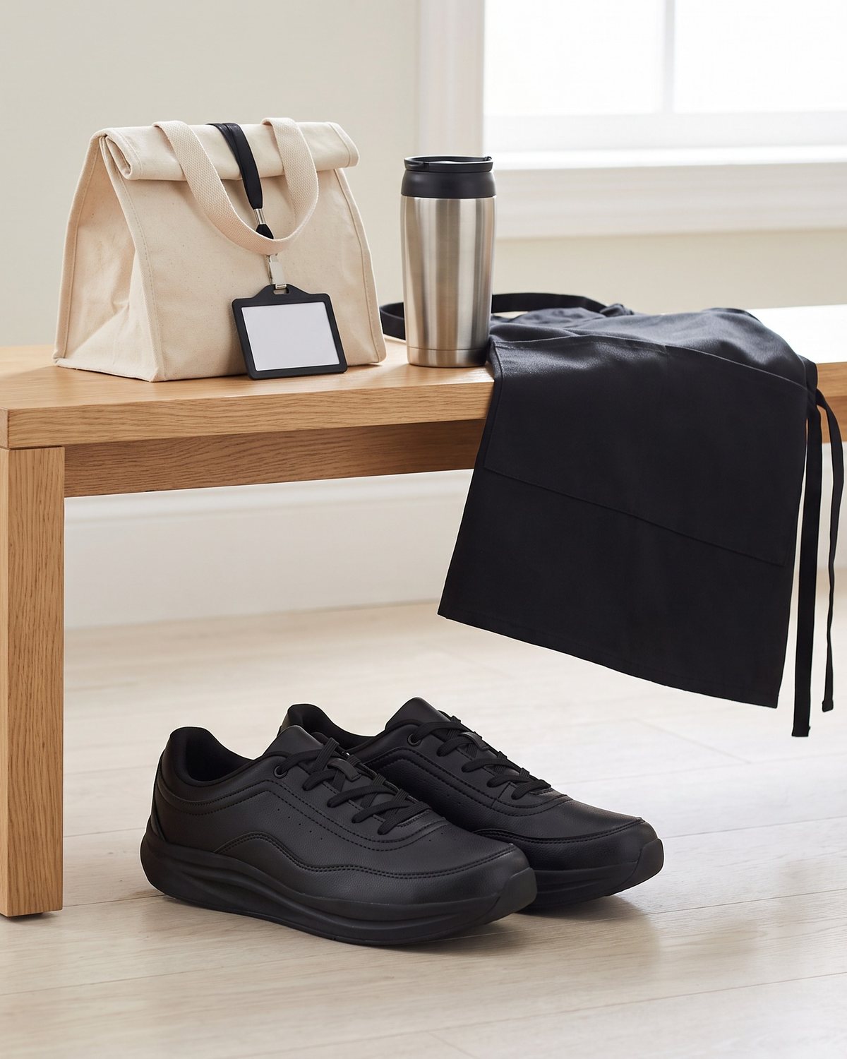 Black Ledger work sneakers under a staff-room bench with a lunch bag and apron