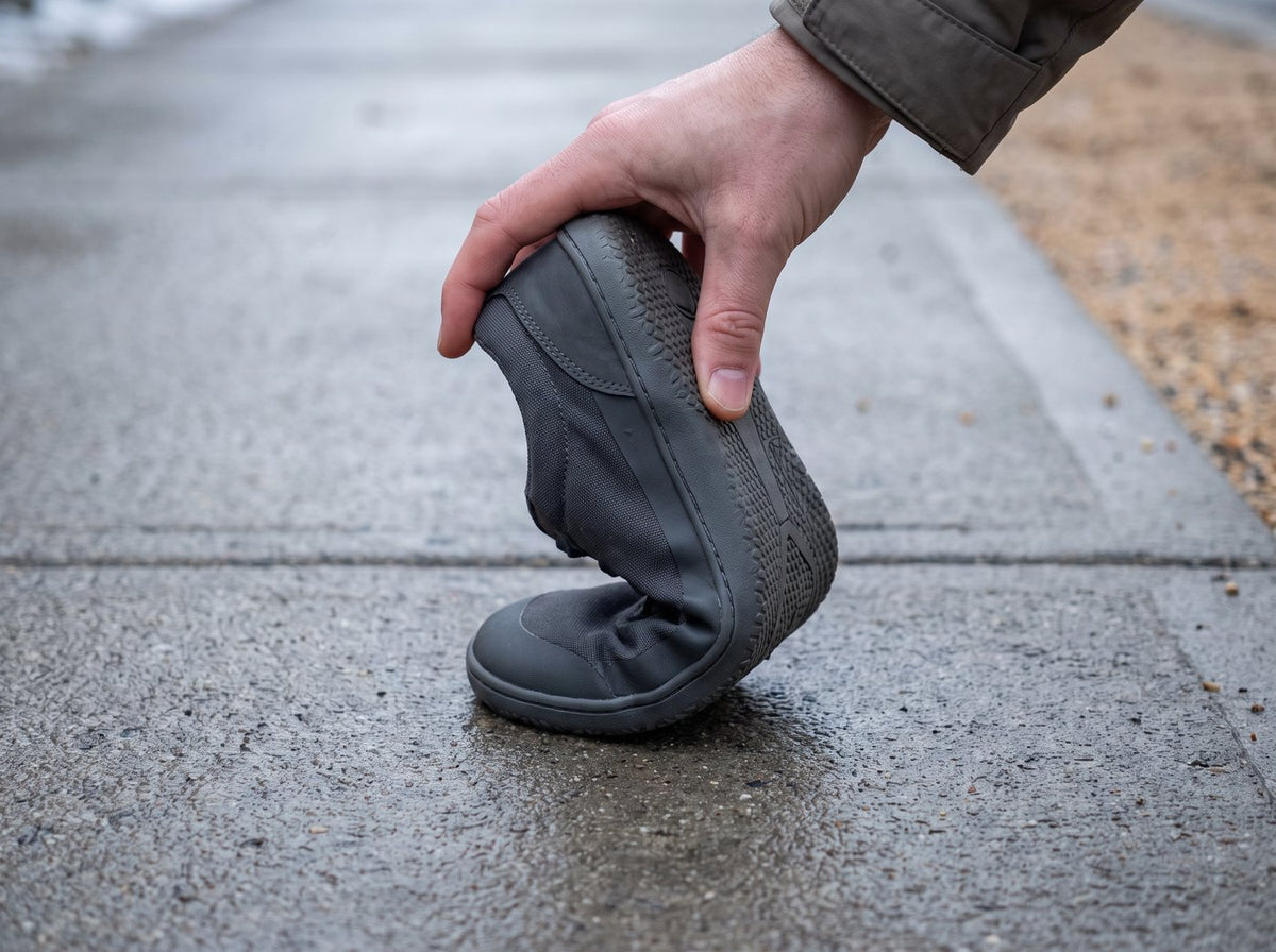 A thin barefoot-style shoe bent in half on a concrete sidewalk
