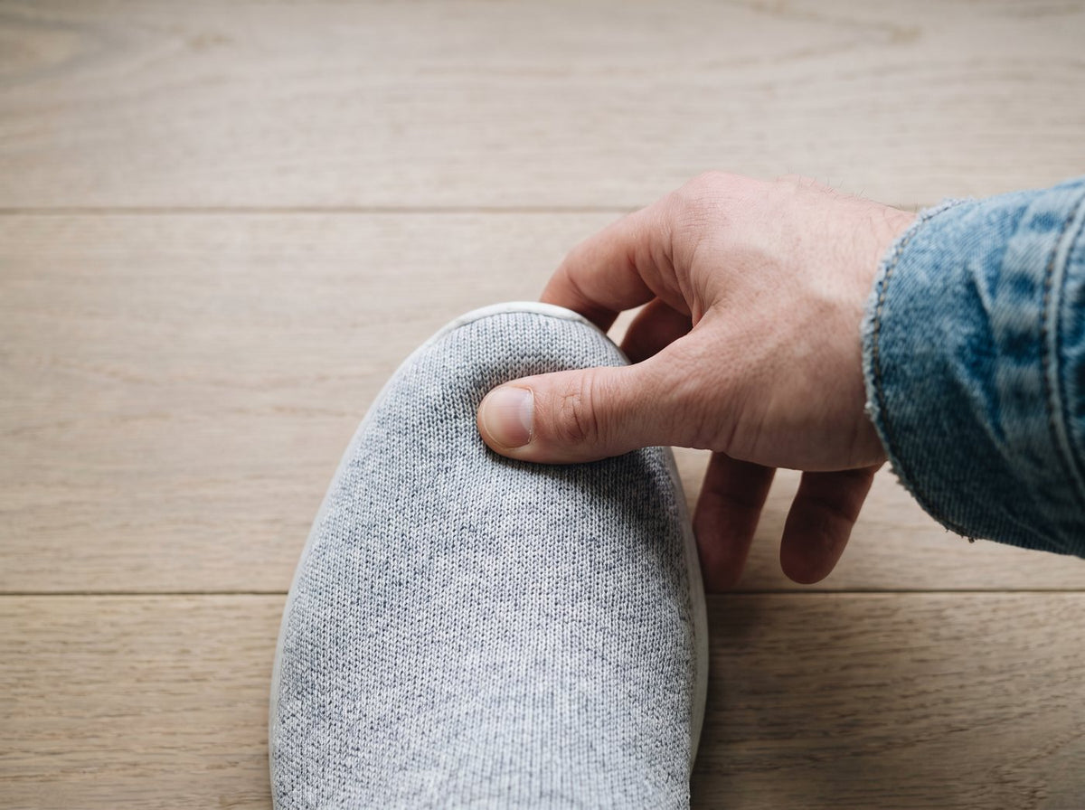 A thumb pressing on the toe of a knit sneaker to check the fit